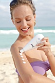 Woman with blond hair applying lotion to her arm on the beach