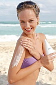 Woman with blond hair applying lotion to her upper arm on the beach