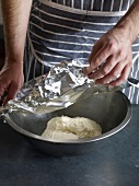 Close-up of hand covering bowl of dough with aluminium foil