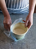 Close-up of hand putting bowl of leaven agent in plastic ziploc bag