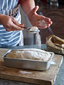 Unbaked bread in a baking tin being dusted with flour