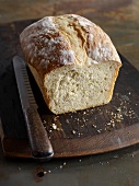 Loaf of white bread with knife on wooden board