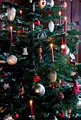 Christmas tree decorated with lit candles, silver jewellery and pine cones