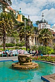 People sitting on benches behind fountain in Central Piazza, Portmeirion village, Wales