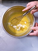 Stirring passion fruit cream and butter in bowl, overhead view