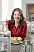 Portrait of pretty woman with brown hair in red blouse eating at restaurant, smiling