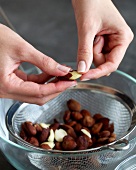 Close-up of hand removing skin from blanched hazelnuts for preparing marzipan, step 1