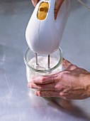 Mixing cream, egg whites and sugar in glass with hand blender
