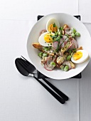Bowl of baked potato salad with broad beans and eggs, overhead view