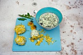 Bowl of green goat cream and balls of goat cream covered with petals on chopping board