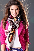 Beautiful woman with dark windswept hair wearing pink jacket and colourful scarf, smiling