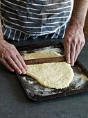 Close-up of rolling dough in baking tray for preparation of fougasse, step 2
