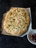 Focaccia bread on baking paper with black olives in bowl