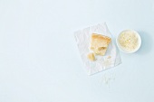 Piece of parmesan on paper and grated parmesan bowl