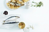 Sardines with sauerkraut on plate, juniper berries in bowl and raw sardines on paper