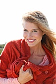 Portrait of beautiful blonde woman with windswept hair wearing red sweater, smiling
