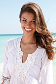 Dark-haired woman in a white blouse laughing by the sea