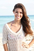 Dark-haired woman in a V-neck mesh sweater, laughing by the sea