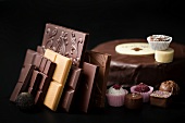 Chocolate bars, chocolates and cake against black background