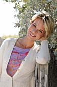 Portrait of pretty blonde woman with short hair wearing top and white cardigan, smiling