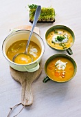 Carrot soup with cream in pot on wooden platter