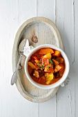 Bowl of pumpkin seitan goulash with spoon on wooden tray