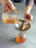 Close-up of pouring jelly from measuring cup through funnel in jar for preparation of jam