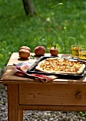 Landküche, Äpfel und Blech mit Zwiebelkuchen auf Tisch, draußen