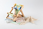 Rolled bill on deck chair, shell, sand and money on white background