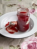 Bottle of rhubarb jelly with strawberries and spoon on plate