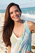 Portrait of beautiful woman with long dark hair wearing top and standing on beach, smiling