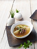 Soup bowl with clear broth, boiled beef, schnittlauch nockerl and herb with vases on table