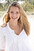 Portrait of beautiful blonde woman wearing white tunic blouse standing on beach, smiling