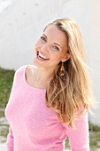Portrait of beautiful blonde woman wearing pink sweater standing near wall, smiling