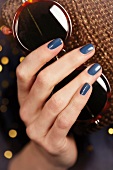 Close-up of woman's hand wearing blue nail paint, holding brown sunglasses