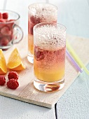 Two glasses of orange juice with diced raspberry