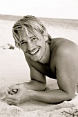 Portrait of happy blonde man having fun while lying on beach, laughing, black and white