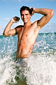 Portrait of happy man with tanned waist having fun in water, hand in hair, smiling