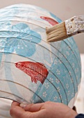 Close-up of person painting colourful lantern with flower and fish motif