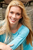 Portrait of beautiful blonde woman with long hair wearing blue top, smiling