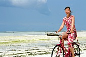 Side view of woman riding bicycle on beach, Zanzibar Island, Tanzania, East Africa