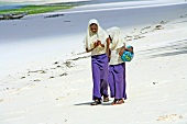 Two girls in uniform walking on beach of Zanzibar, Tanzania, East Africa