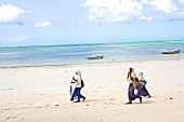 Three girls in uniform walking on beach of Zanzibar, Tanzania, East Africa