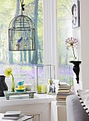 A bird cage, a wall console, a picture on the wall and various decorative objects on the window sill in the corner of the room