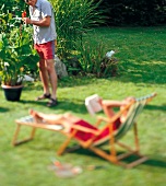 Weekend Gärtner, Paar relaxt im Garten, Frau in Liege liest Buch