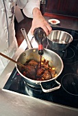 Chef pouring wine in braised pork cheeks in pan