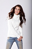 Portrait of pretty woman with dark hair in white turtleneck sweater and jeans, smiling