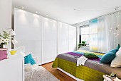 Schlafzimmer mit Schrankwand & Doppelbett mit bunter gesteppter Tagesdecke