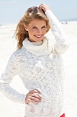 Portrait of blonde woman wearing white turtleneck sweater standing on beach, smiling