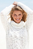 Portrait of blonde woman wearing white turtleneck sweater standing on beach, smiling